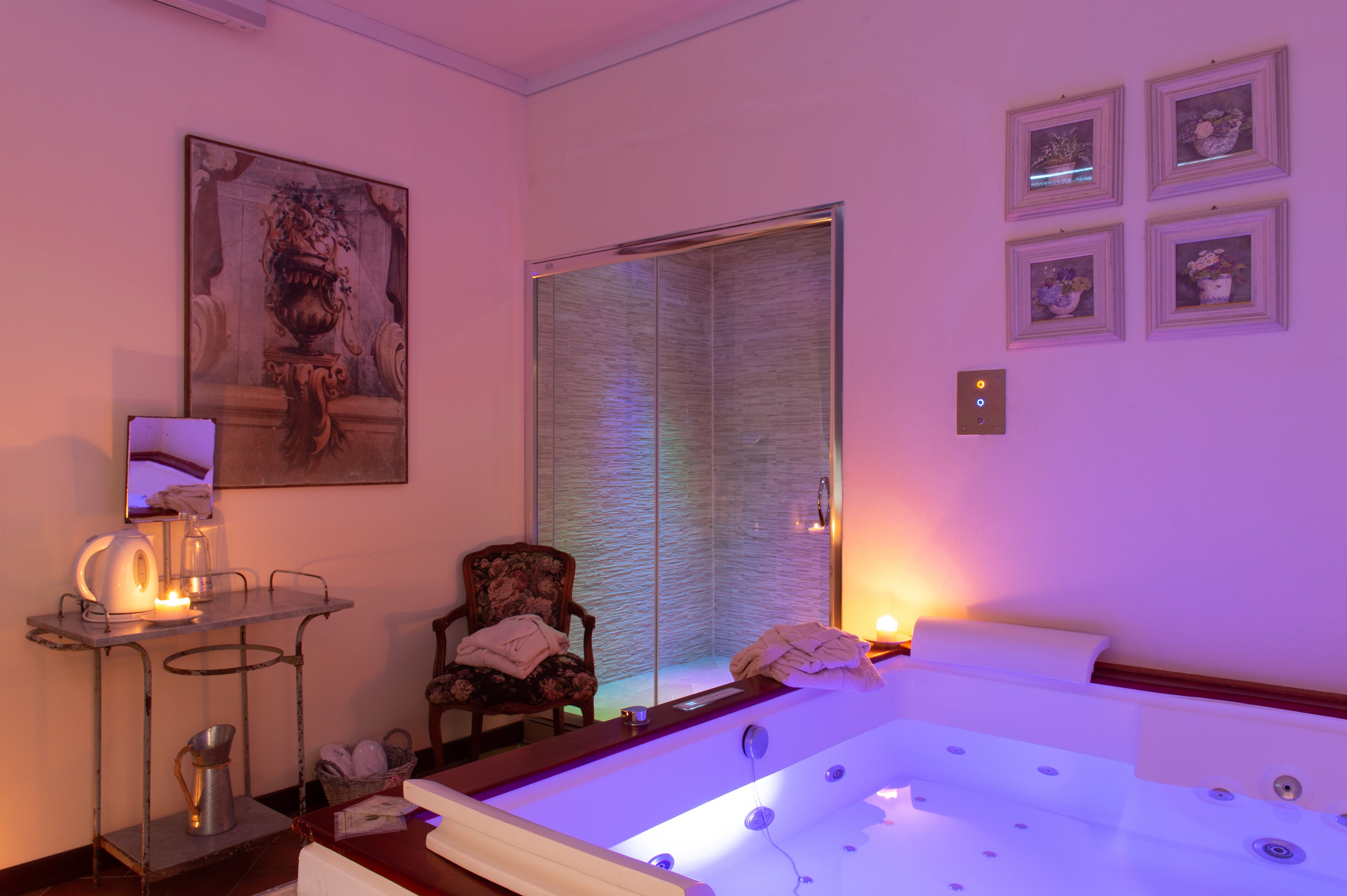 A spa room with a large bathtub, a chair, a small table with a candle, and a painting on the wall.