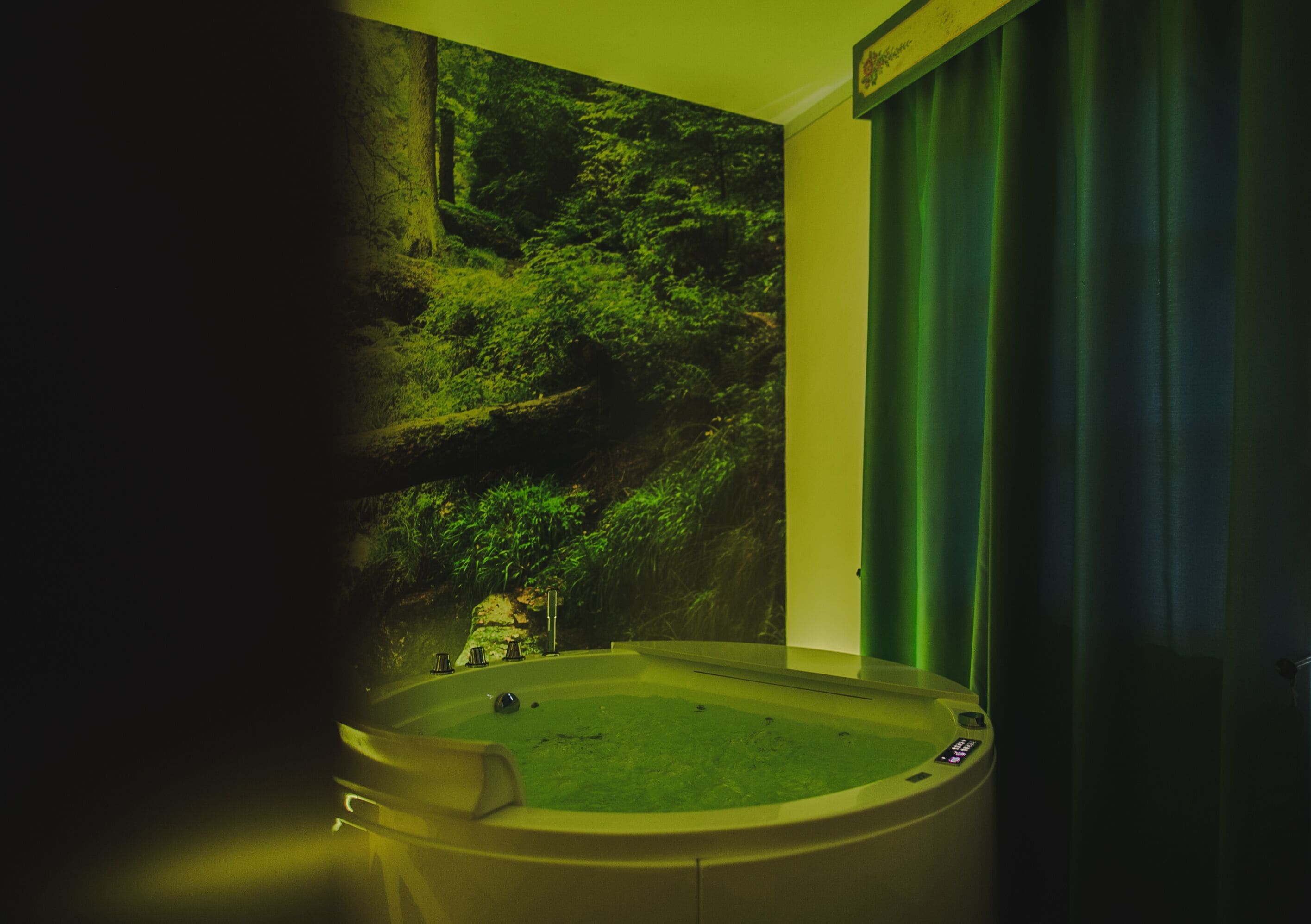 Un bagno con una vasca da bagno ampia, una tenda verde e un affresco raffigurante una scena di bosco.