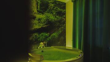 Un bagno con una vasca da bagno ampia, una tenda verde e un affresco raffigurante una scena di bosco.