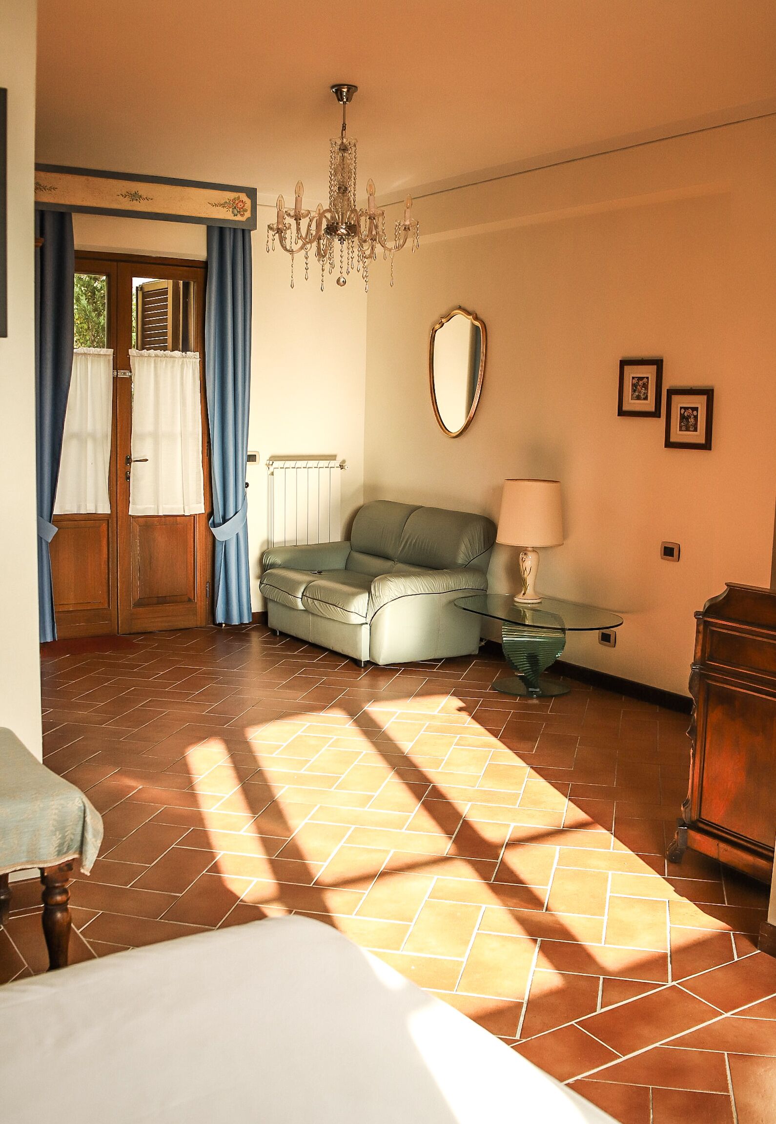 A room with a sofa, a glass table with a lamp, a wooden cabinet, and a door with curtains.