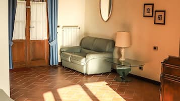 A room with a sofa, a glass table with a lamp, a wooden cabinet, and a door with curtains.