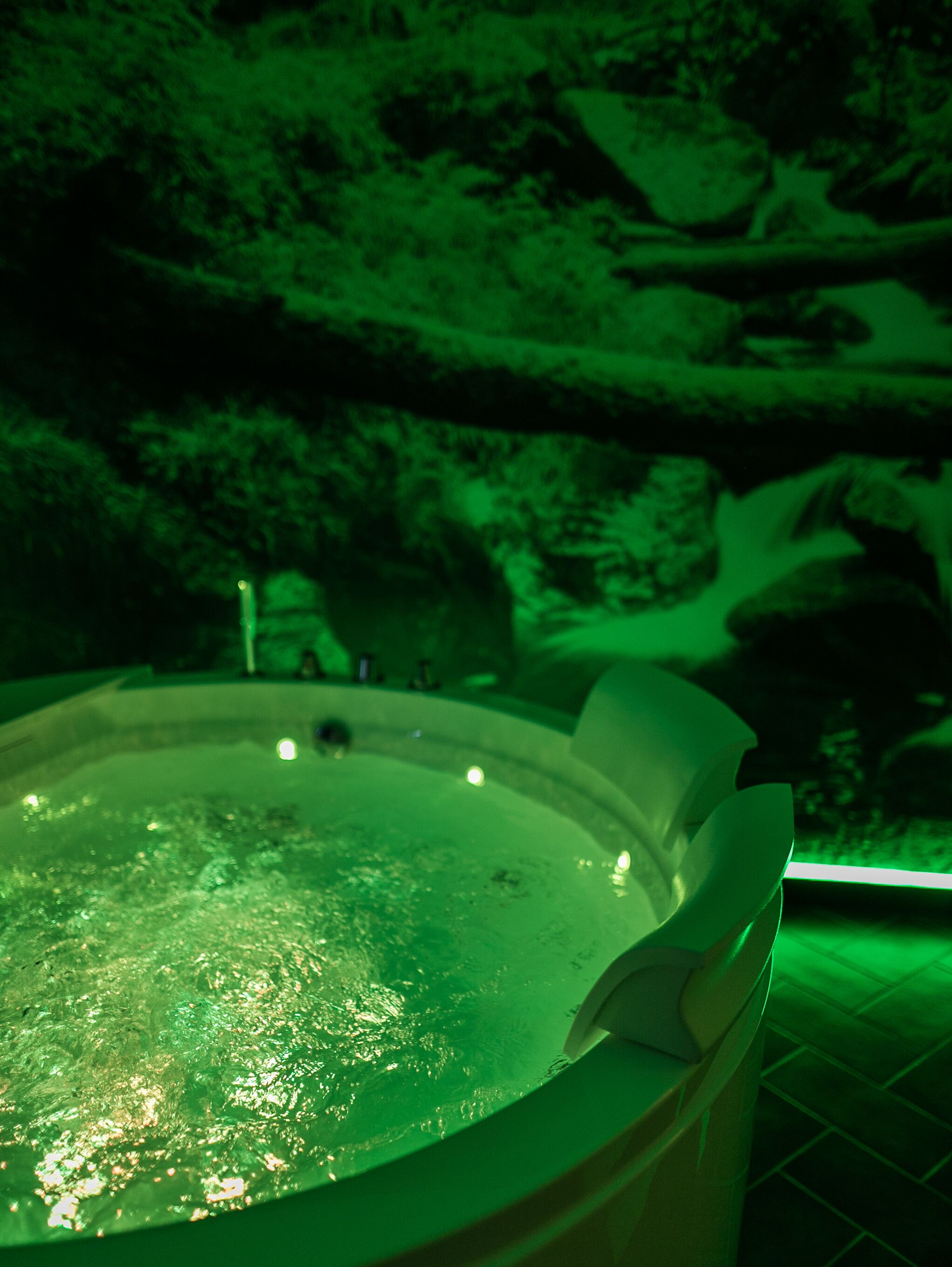 Un bain à remous dont l’intérieur est illuminé de lumière verte, entouré d’une structure ressemblant à un rocher.