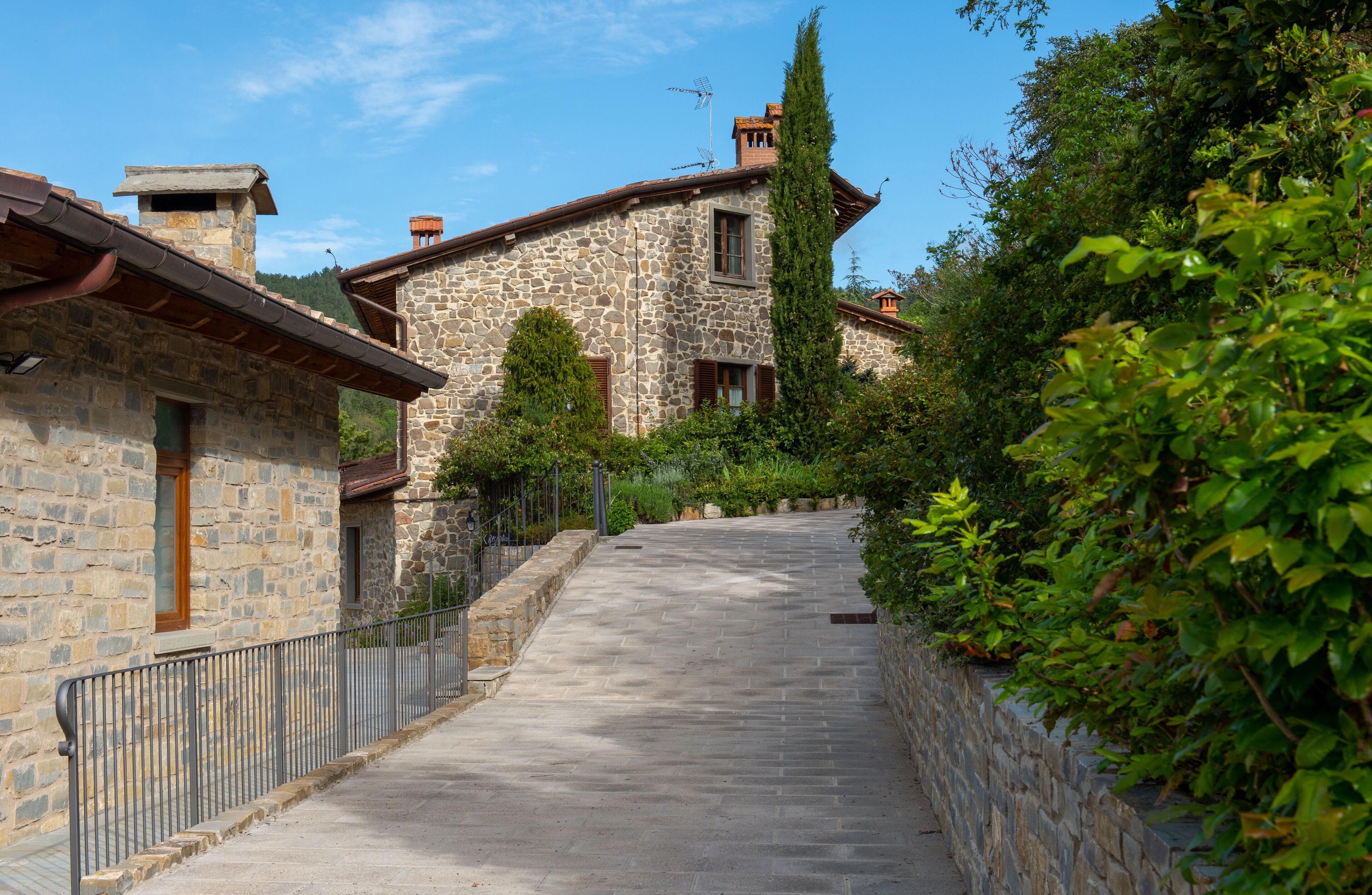 Un bâtiment en pierre avec un toit en pente, un chemin pavé et un mur en pierre d’un côté.