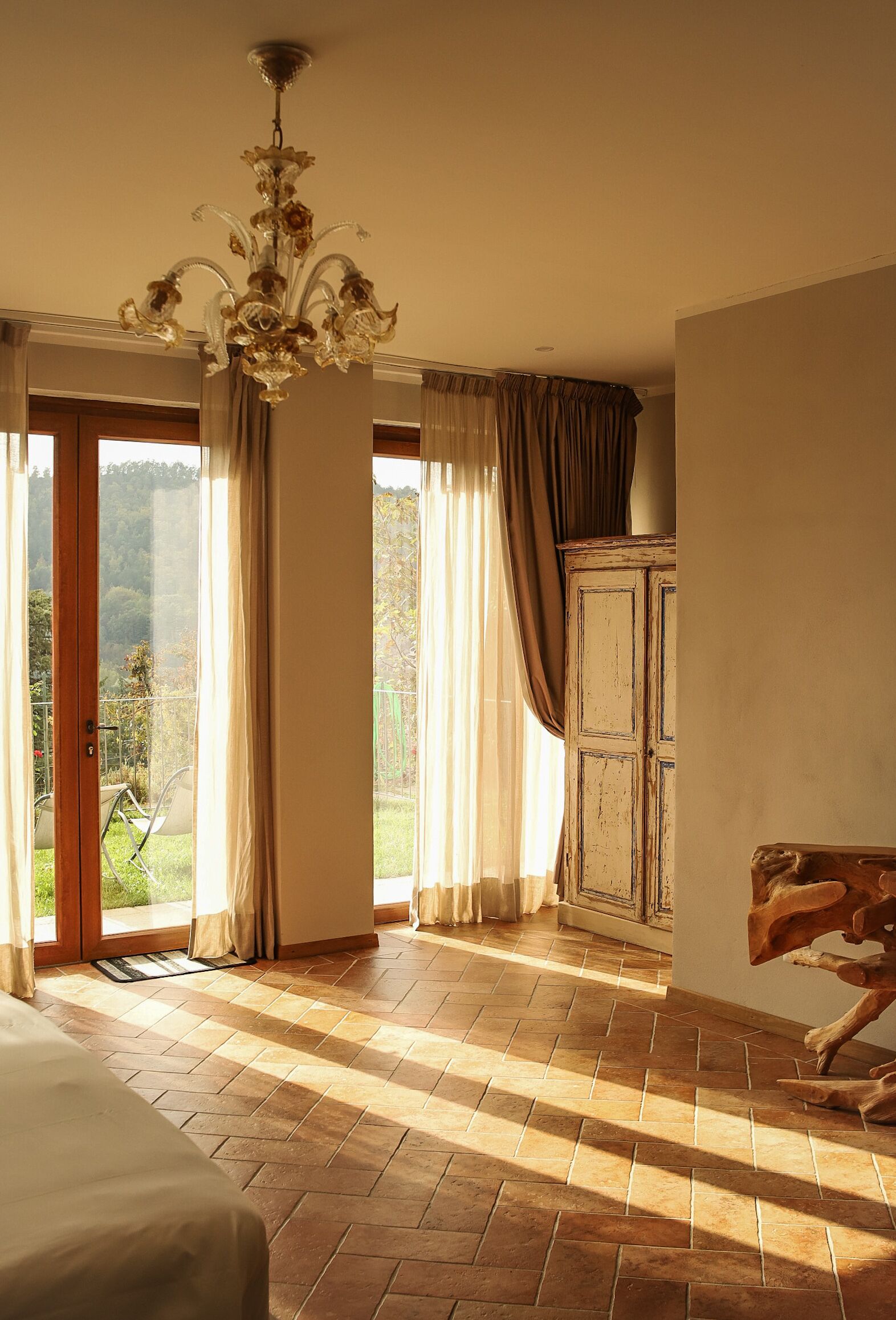 A spacious room with a large window, a wooden cabinet, and a chandelier.
