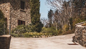 A stone building with a chimney, a tall evergreen tree, and a paved pathway. - Borgo I Tre Baroni (Poppi)