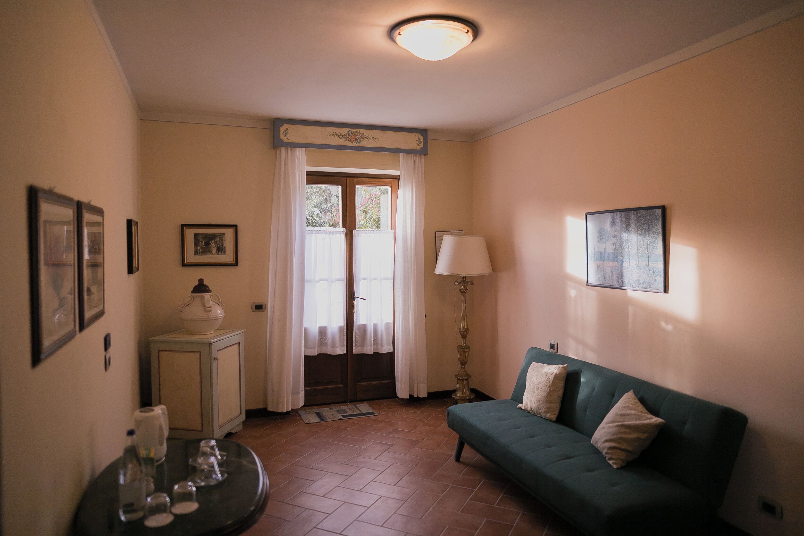 A room with a green sofa, a small table with glasses, a cabinet, a lamp, and a door with curtains.