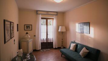 Una habitació amb un sofà verd, una taula petita amb gots, un armari, una làmpada i una porta amb cortines.