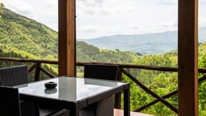 A wooden deck with a glass table and wicker chairs overlooking a mountainous landscape. - Borgo I Tre Baroni (Poppi)