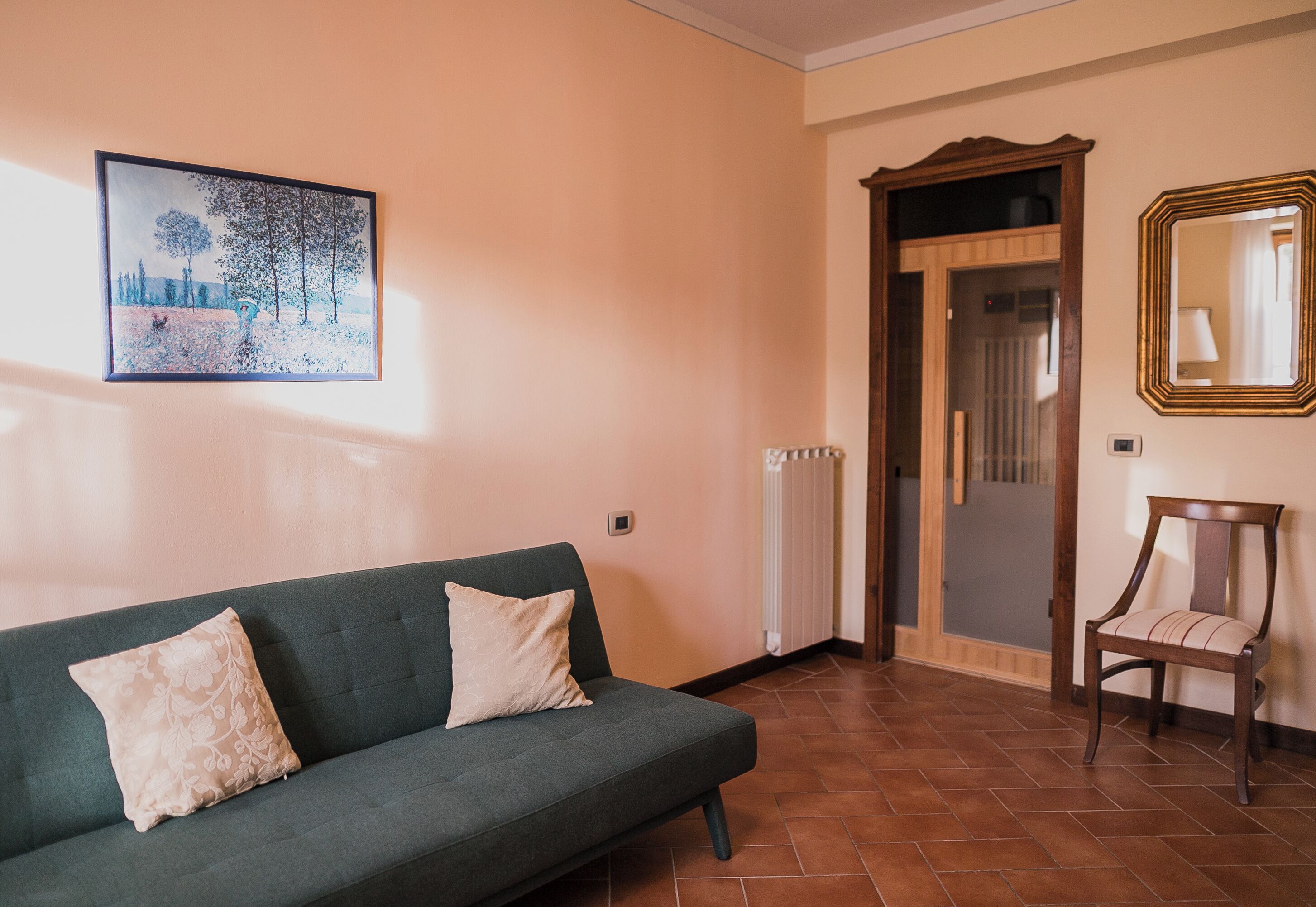 Una stanza con un divano verde, una sedia di legno, un quadro incorniciato e una porta che dà su un'altra stanza.