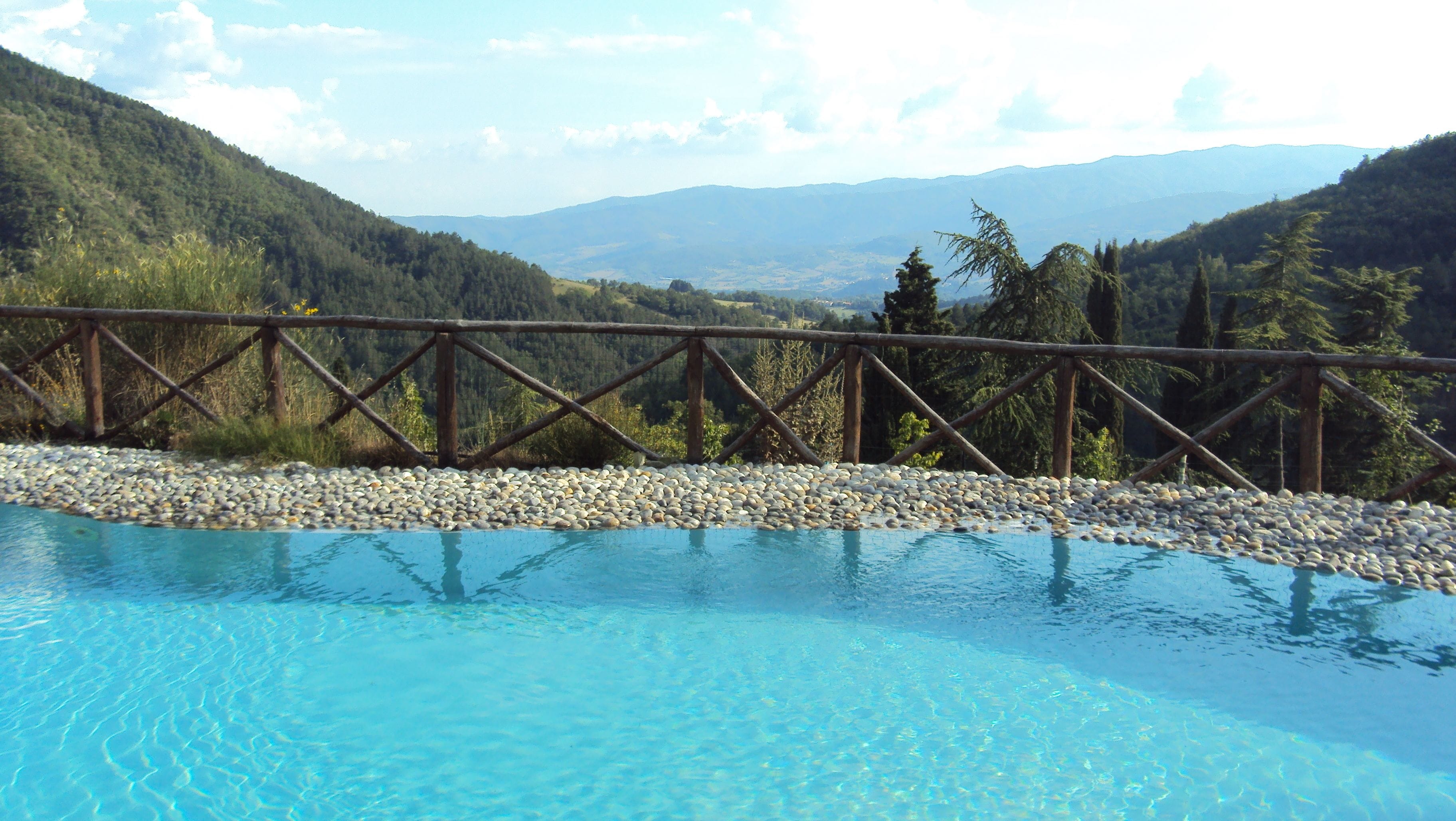 Una piscina amb una terrassa de fusta i vista a un paisatge muntanyós.