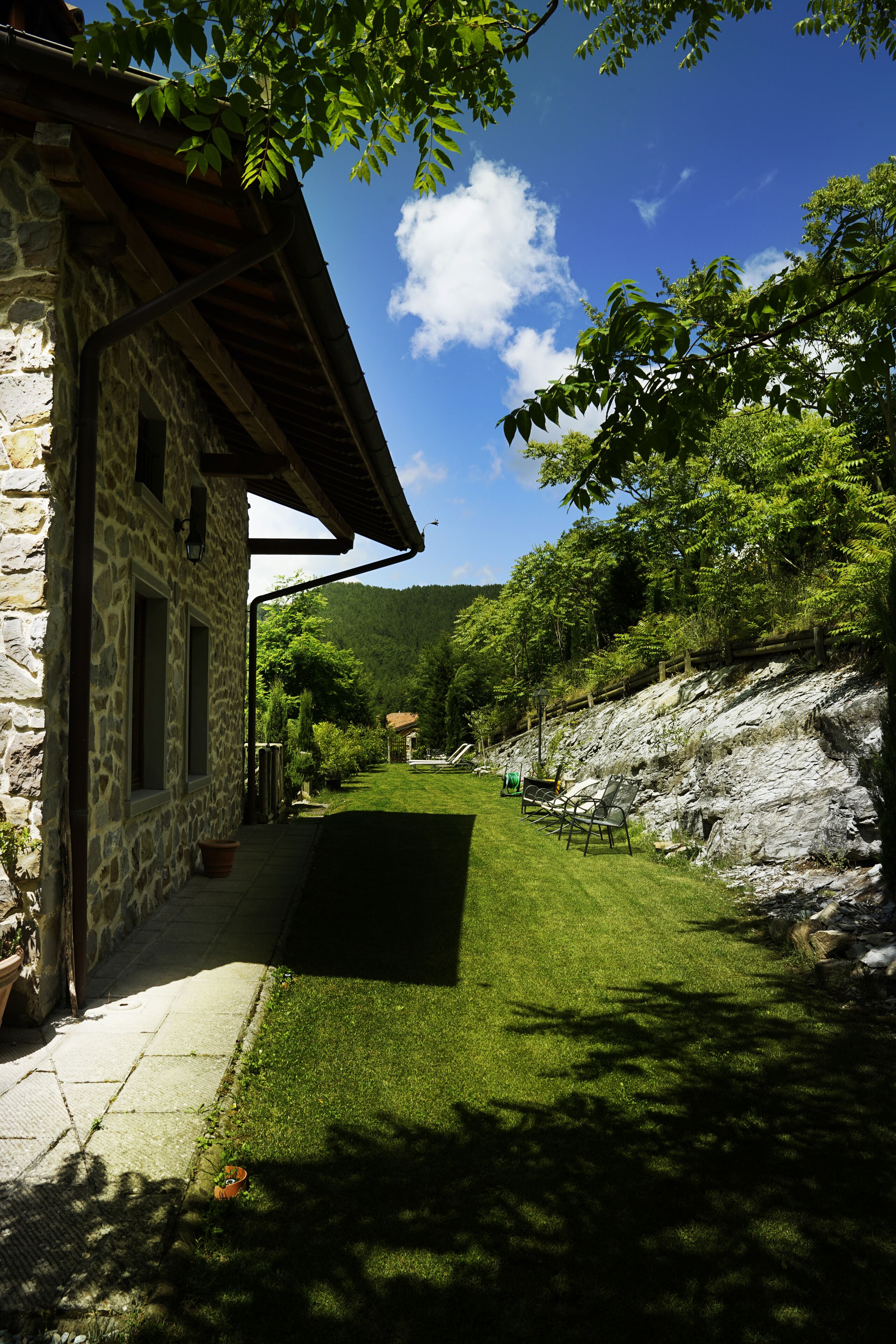 Un edificio de piedra con techo inclinado, un sendero empedrado y un área verde con bancos.
