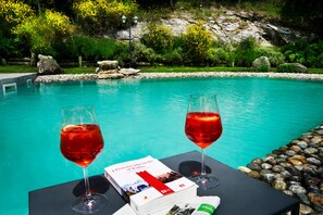 A poolside setting with two glasses of red wine, a book, and a menu on a table. - Borgo I Tre Baroni (Poppi)