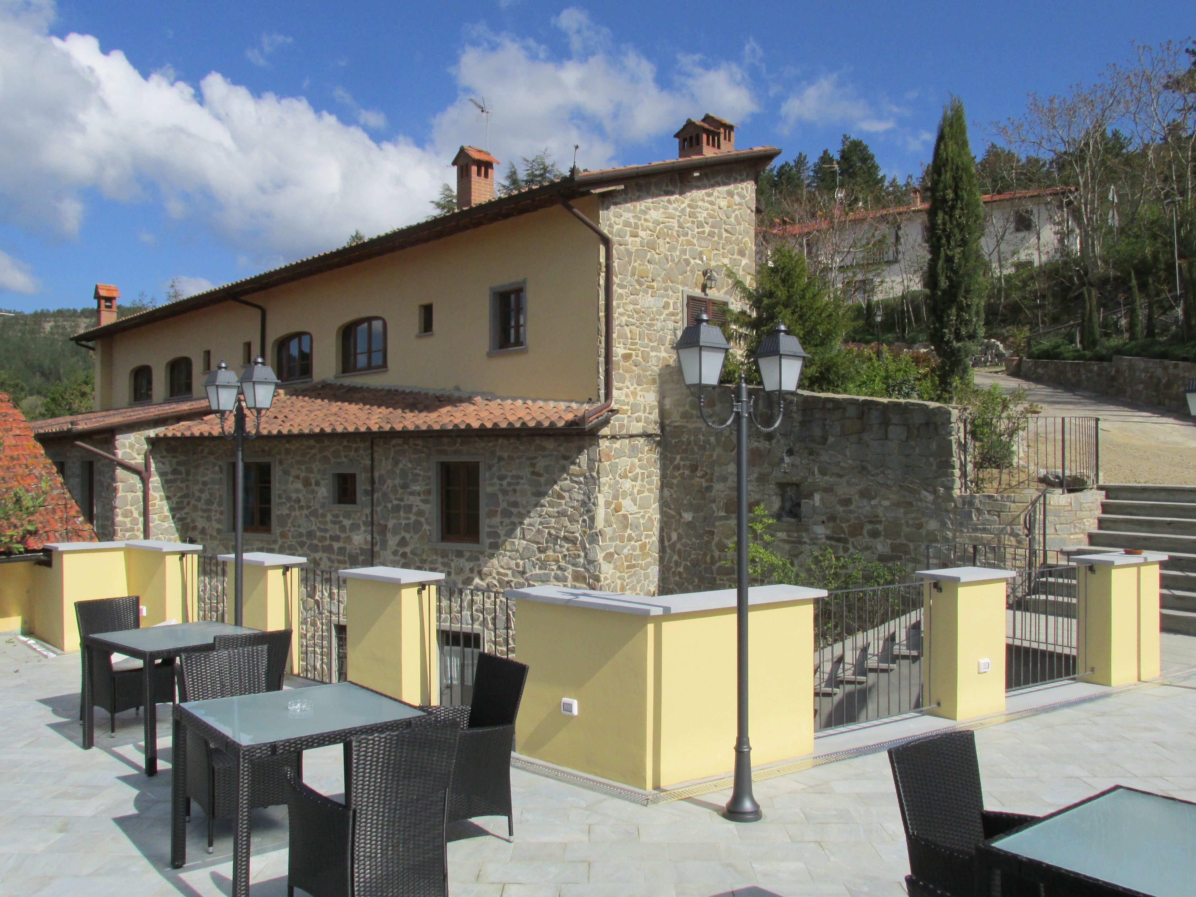 An outdoor patio area with stone walls, a yellow building, and outdoor furniture.