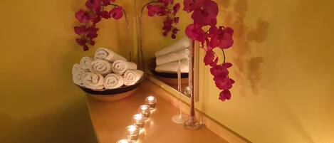 A spa area with a wooden bench, a bowl of rolled towels, and pink orchids.