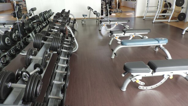 Uma academia com diversos equipamentos de musculação, bancos e espelhos.