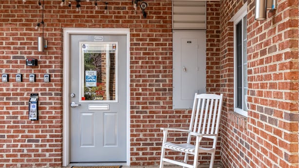 A brick building with a white door, a white rocking chair, and a mailbox. - Affordable Suites of America Harrisonburg (Harrisonburg)