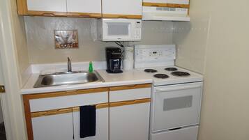 A compact kitchen with a sink, a coffee maker, a microwave, and a stove.