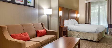 Habitación de hotel con sofá, cama, mesita de noche, lámpara y cuadros en la pared.