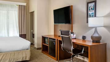 A hotel room with a bed, desk, chair, television, and a lamp.