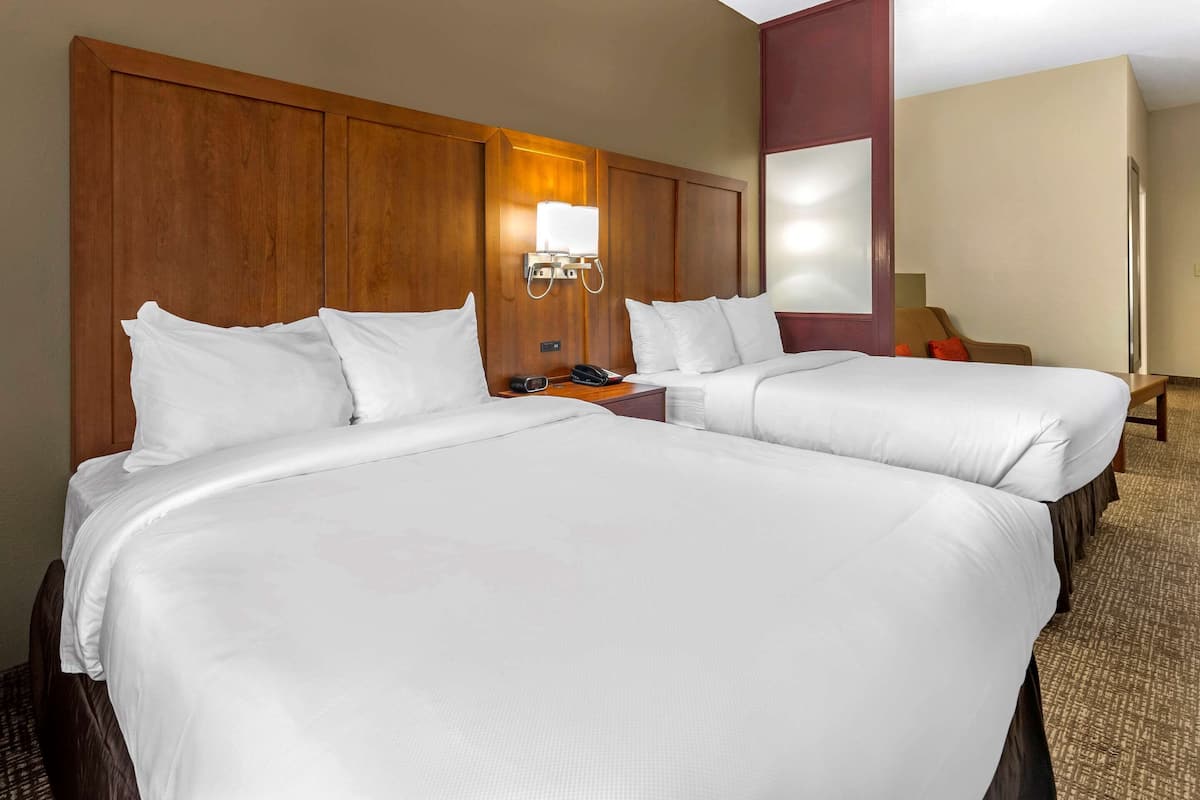 A hotel room with two large beds, a wooden headboard, a nightstand with a phone, and a wall-mounted light fixture.