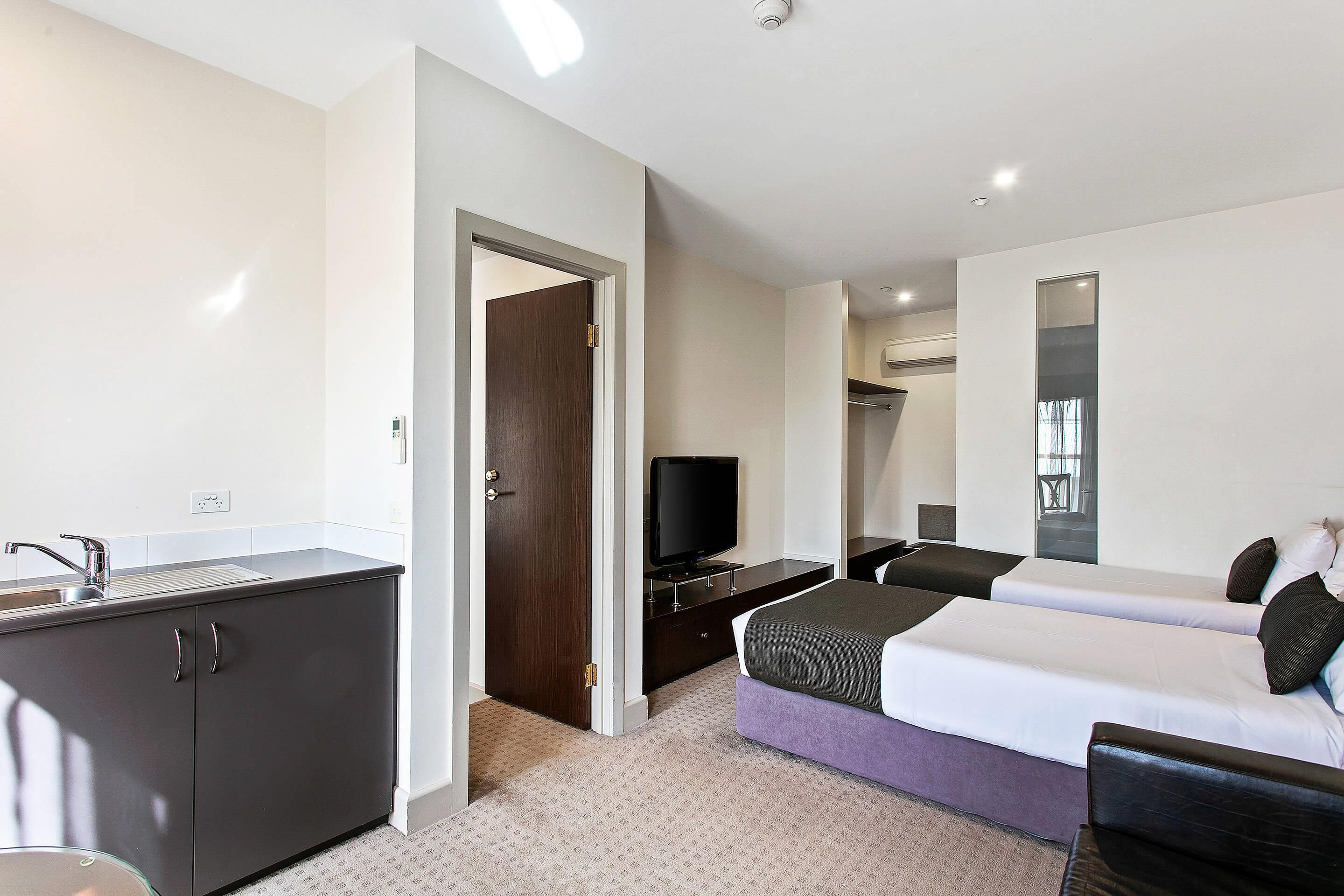 A hotel room with a bed, a TV, a desk with a sink, and a wardrobe.