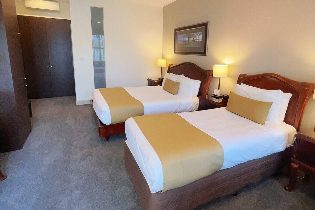 A hotel room with two beds, a wardrobe, a desk, and a framed picture on the wall.