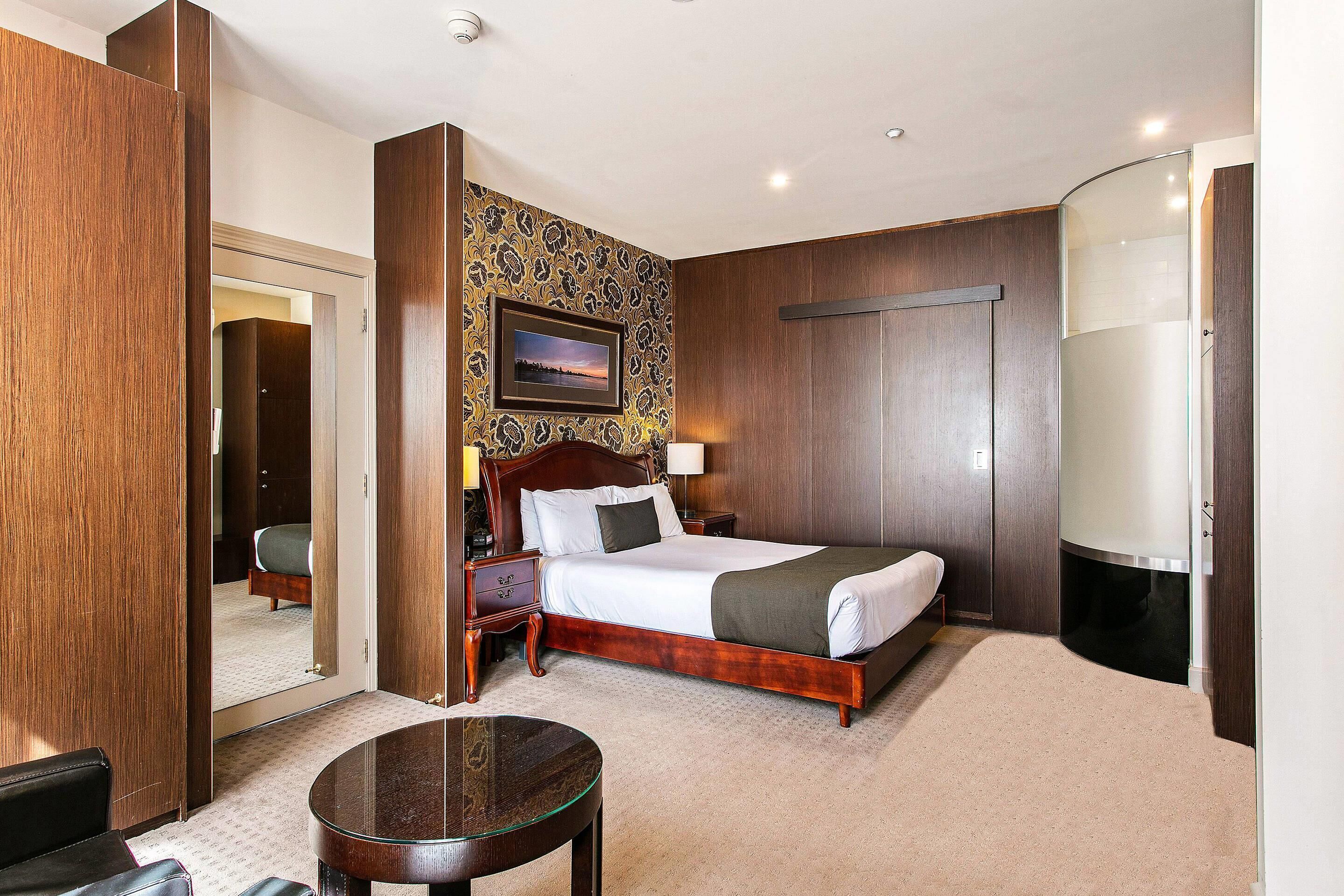 A hotel room with a large bed, a bedside table, a mirror, a round table, and a wardrobe.
