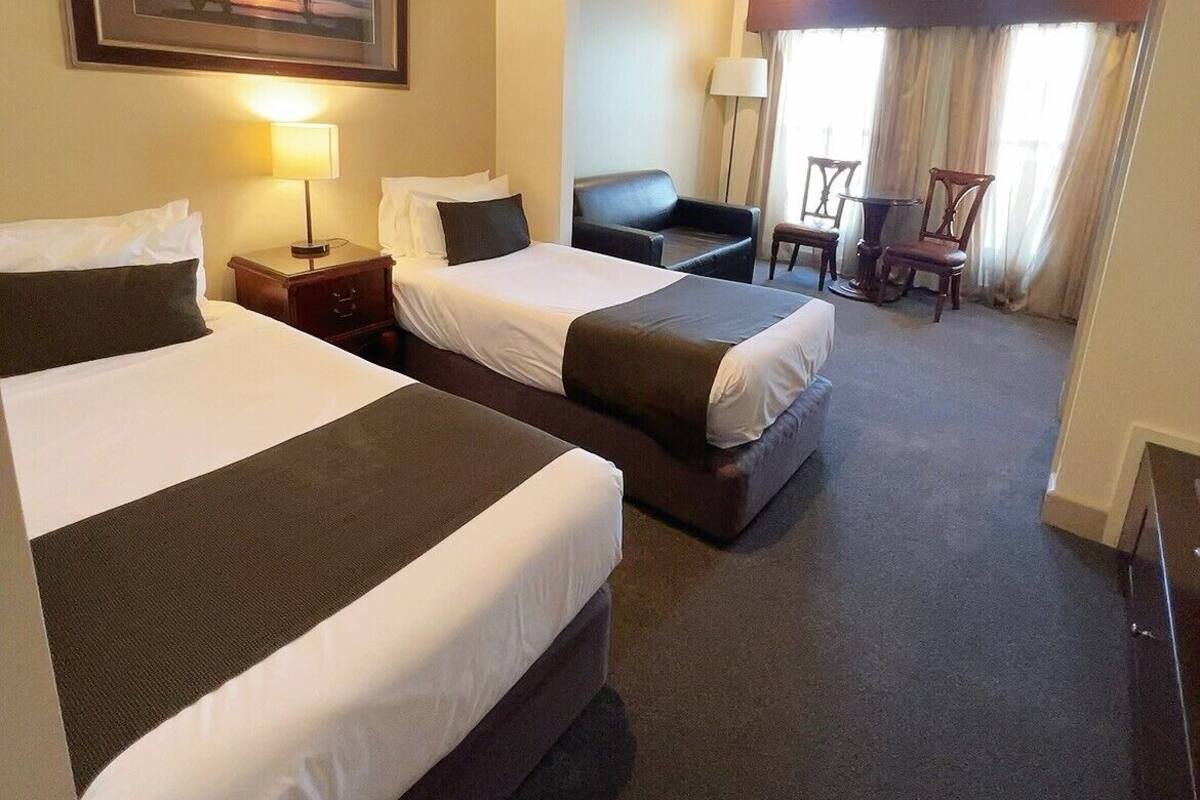 A hotel room with two beds, a desk, a chair, a lamp, and a painting on the wall.