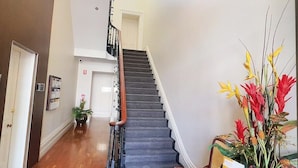 A grand staircase with a chandelier, a wooden floor, and a table with a floral arrangement.