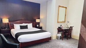 A hotel room with a large bed, a desk, a chair, a mirror, and a chandelier.