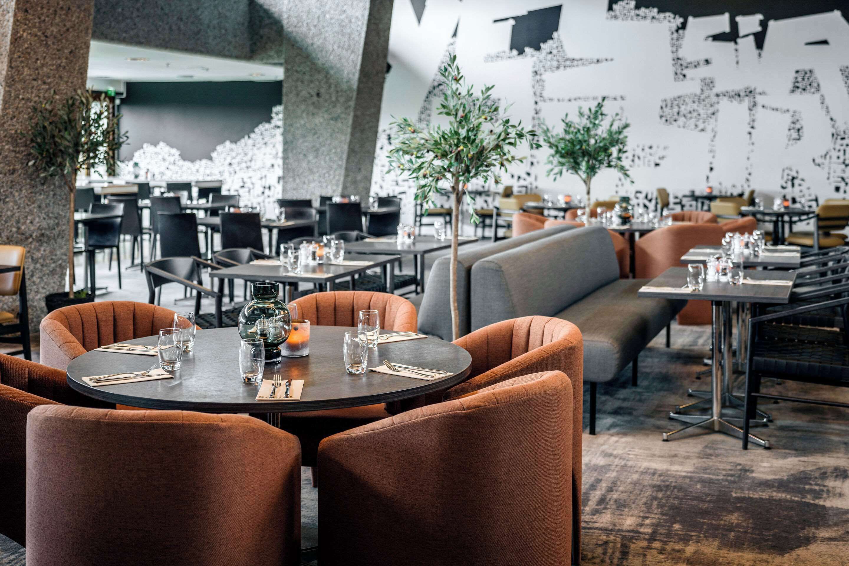 Un ristorante moderno con tavoli rotondi e sedie arancioni, caratterizzato da un arredamento minimalista e un'ampia opera d'arte astratta a parete.