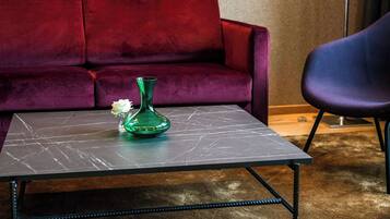 A room with a dark marble table, a green vase with white flowers, a red velvet sofa, and a blue chair.