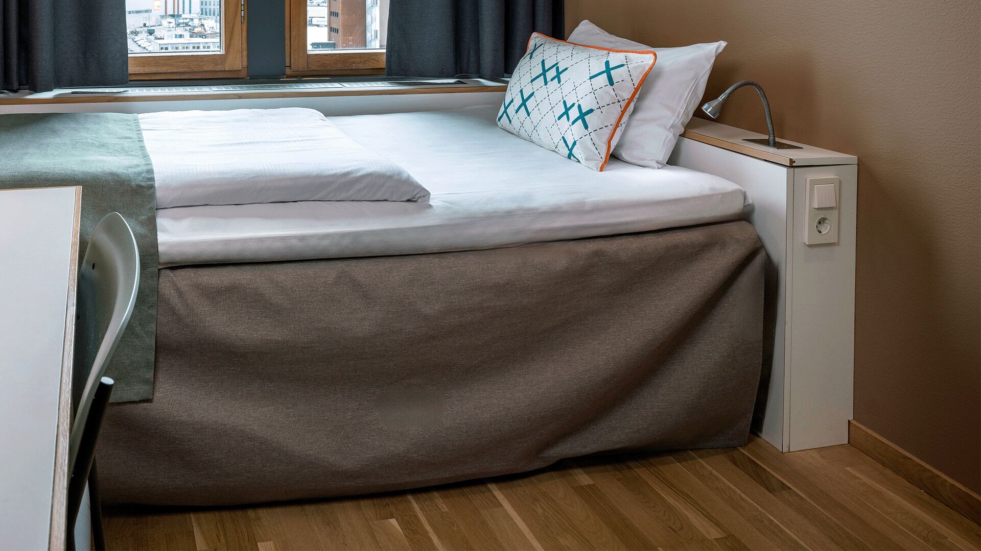 Un lit compact avec une housse grise, un matelas blanc et un oreiller à motifs bleus.