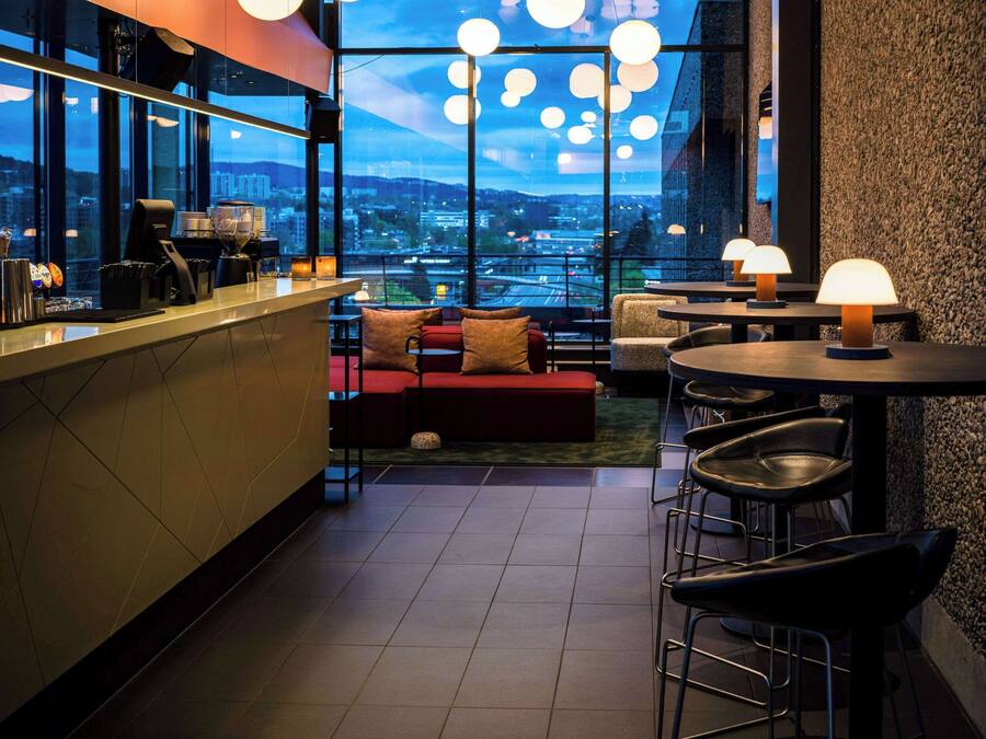 A modern bar area with a city view, bar stools, and a seating area with a red sofa.