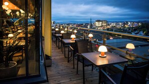 An outdoor dining area with tables and chairs, a railing, and a city view in the background. - Quality Hotel 33 (Oslo)