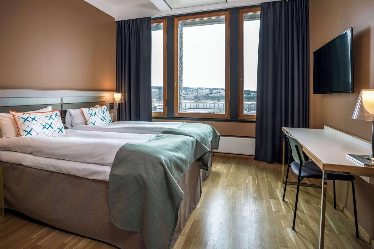 A hotel room with a bed, a desk, a chair, and a TV on the wall.
