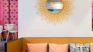Un intérieur moderne avec un motif géométrique sur le mur, un miroir rond et un canapé agrémenté de coussins.