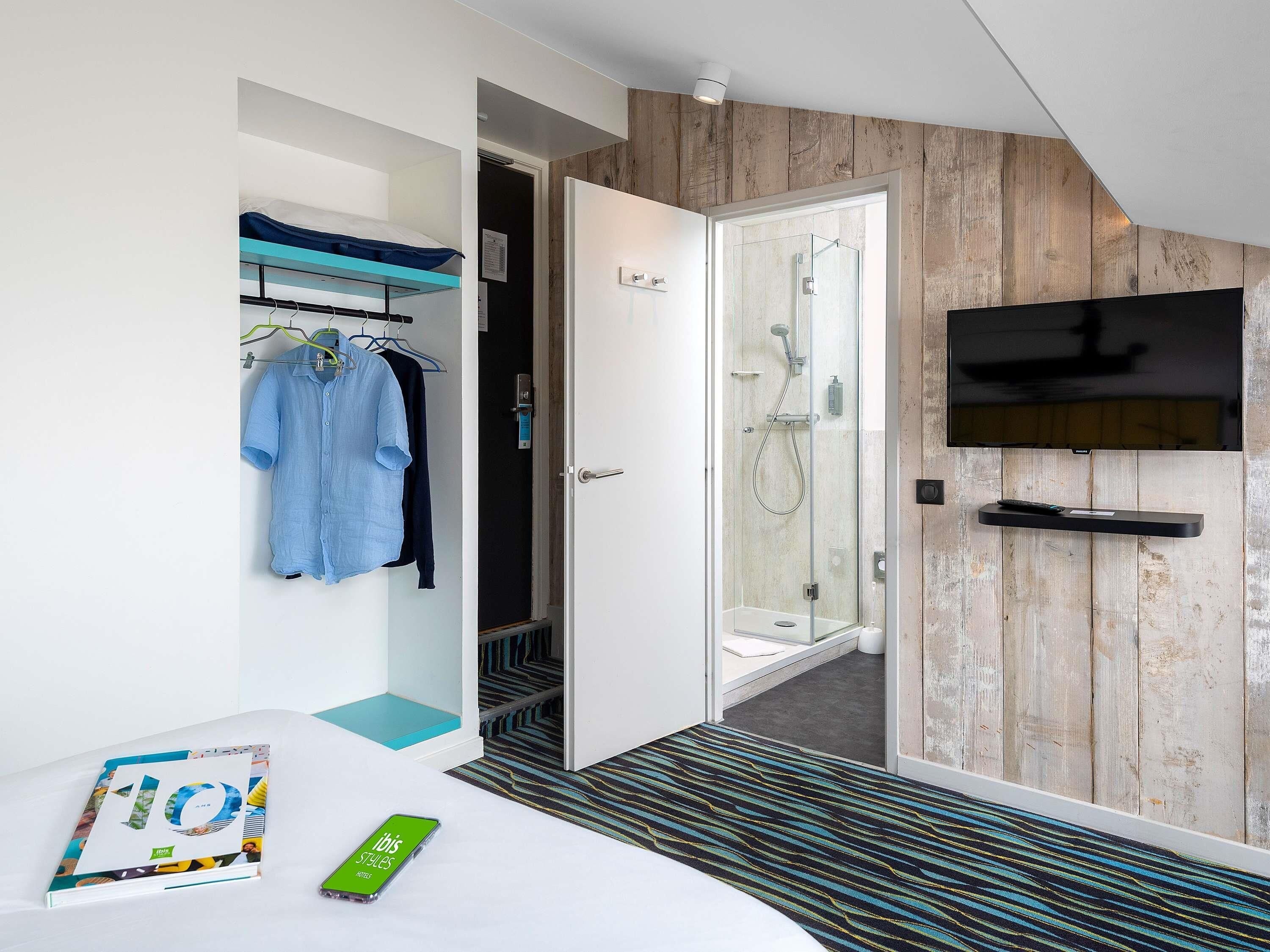A hotel room with a bed, a wardrobe, a shower area, and a mounted television.
