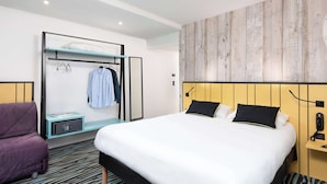 A modern hotel room with a large bed, a built-in wardrobe, a seating area with a purple chair, and a wooden accent wall. - ibis Styles Macon Centre (Macon)