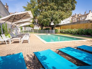 A pool area with lounge chairs and umbrellas, surrounded by a brick patio and greenery. - ibis Styles Macon Centre (Macon)
