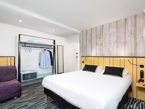 Une chambre d’hôtel comprenant un lit, un coin salon, une armoire et un téléphone fixé au mur.