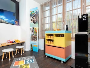 A room with a colorful cabinet, a black refrigerator, wooden stools, a poster on the wall, and a window with curtains. - ibis Styles Macon Centre (Macon)