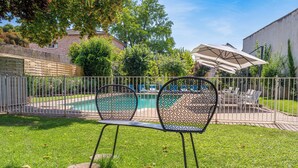 Un jardin avec une piscine, deux chaises en métal, une table et un grand parasol.