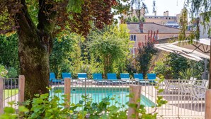 A pool area with blue lounge chairs, a tree, and a building in the background. - ibis Styles Macon Centre (Macon)