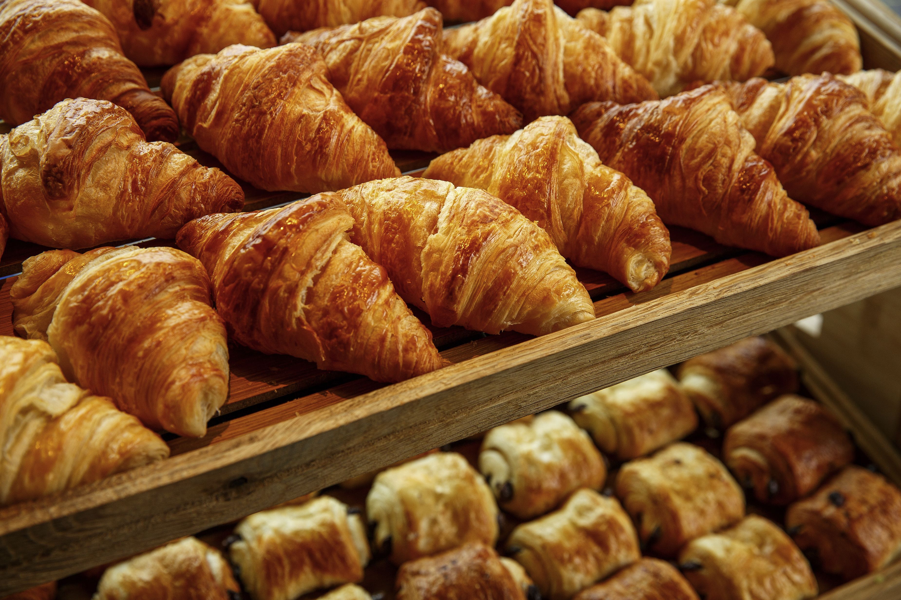 Un plateau en bois rempli d’une variété de viennoiseries, notamment des croissants et des pâtisseries fourrées au chocolat.