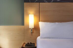 A neatly made bed with white linens and a wooden headboard. A bedside table with a lamp and a pair of glasses is visible. - ibis London Elstree Borehamwood (Borehamwood)