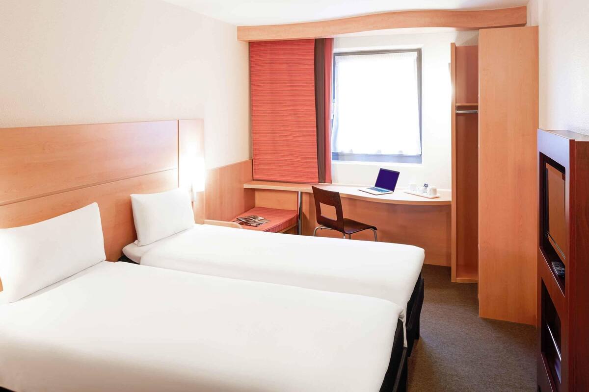 Et hotelværelse med to senge, et skrivebord med en bærbar computer, en stol og et skab.