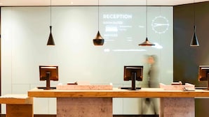 Un mostrador de recepción con pantalla digital, iluminación colgante y un ventanal grande.