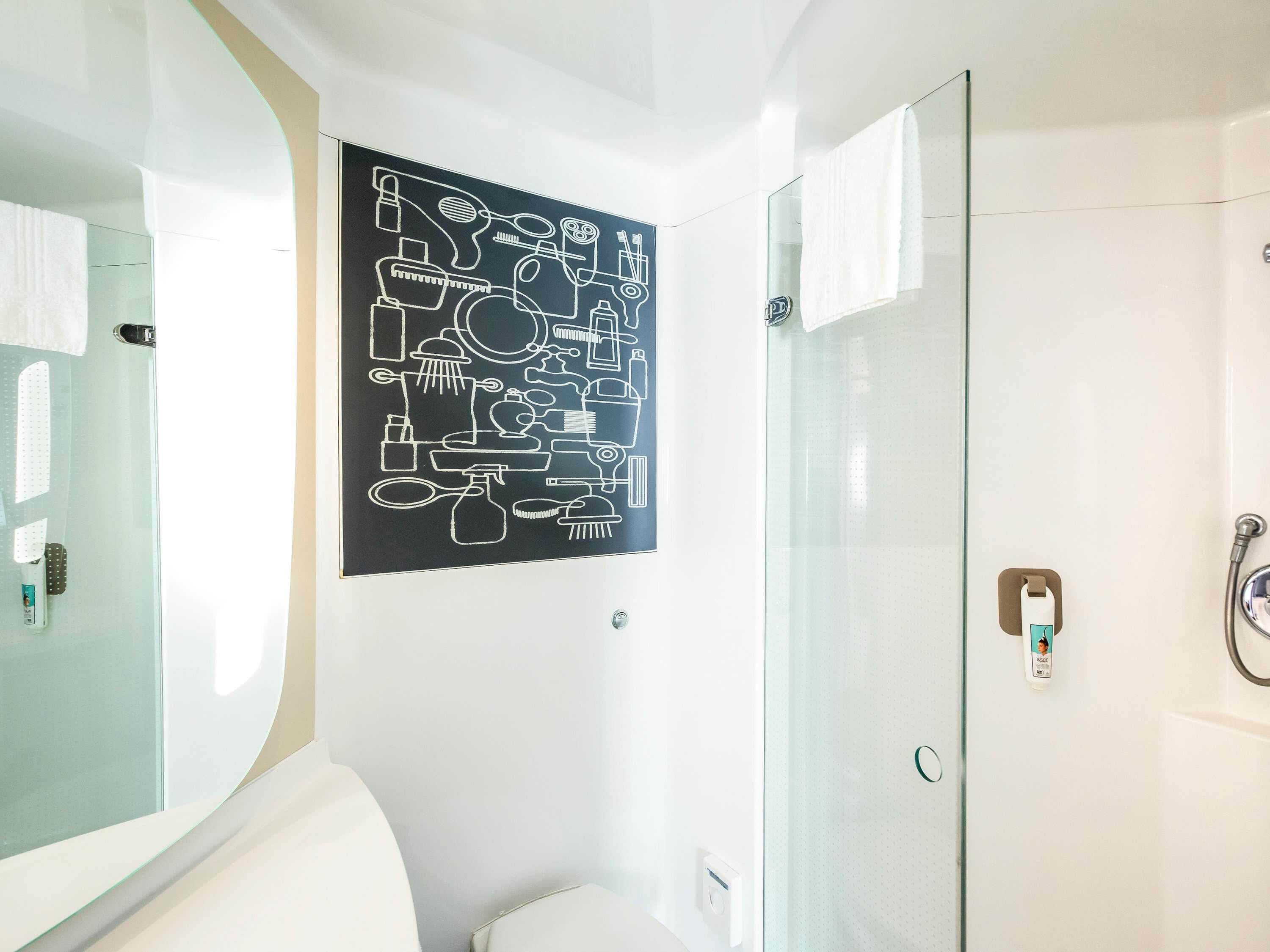 Une salle de bain avec une porte de douche en verre, des toilettes blanches et une œuvre d’art abstraite en noir et blanc accrochée au mur.