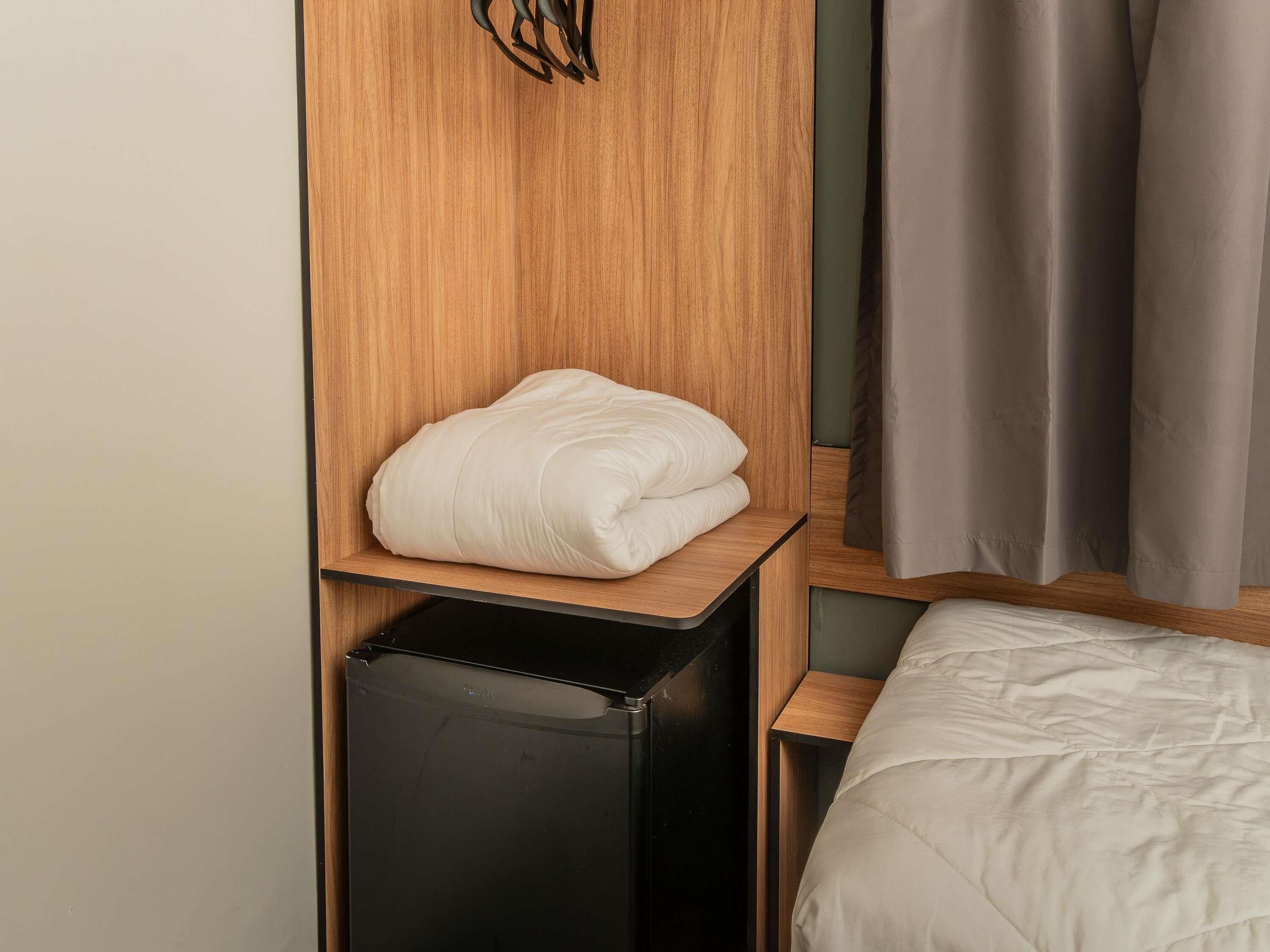A neatly made bed with a white duvet, a wooden headboard, and a black nightstand with a drawer.